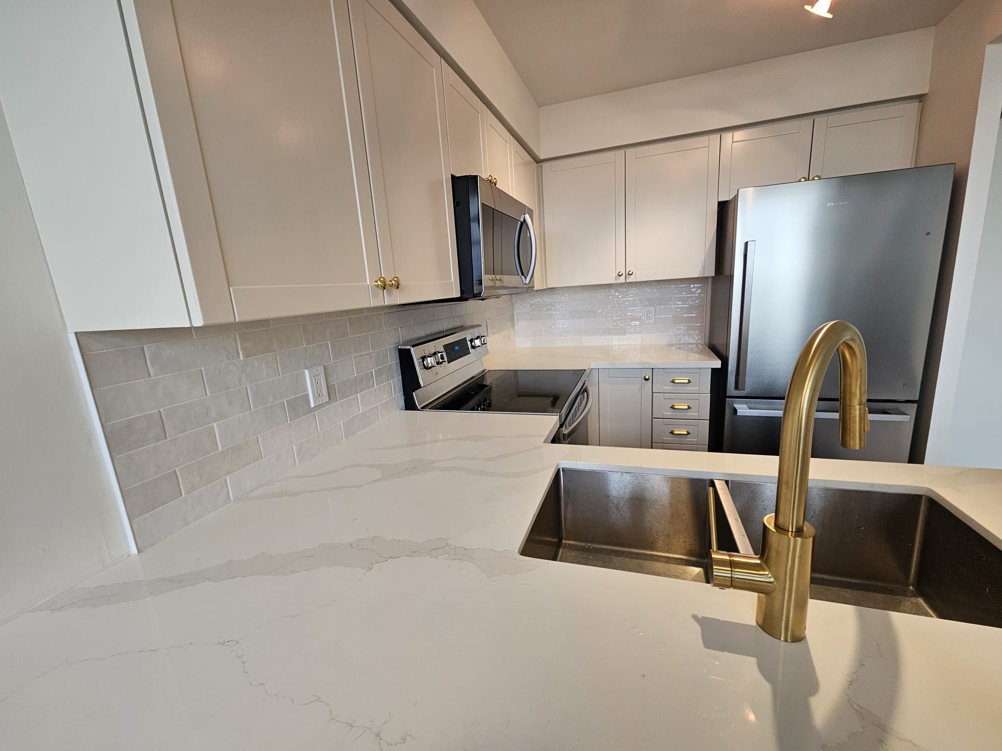 Modern white kitchen with stainless appliances and brass faucet