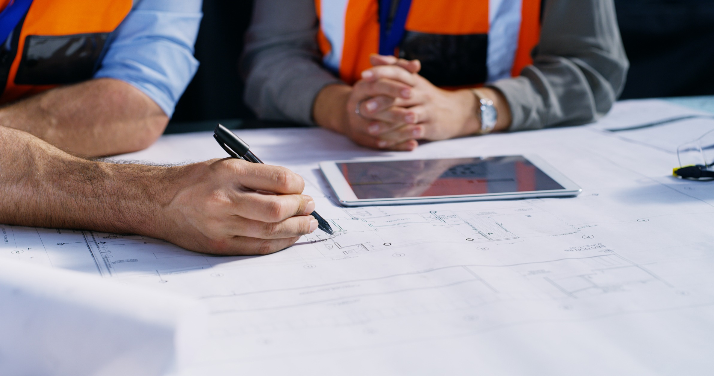 Engineers reviewing blueprints with tablet at table