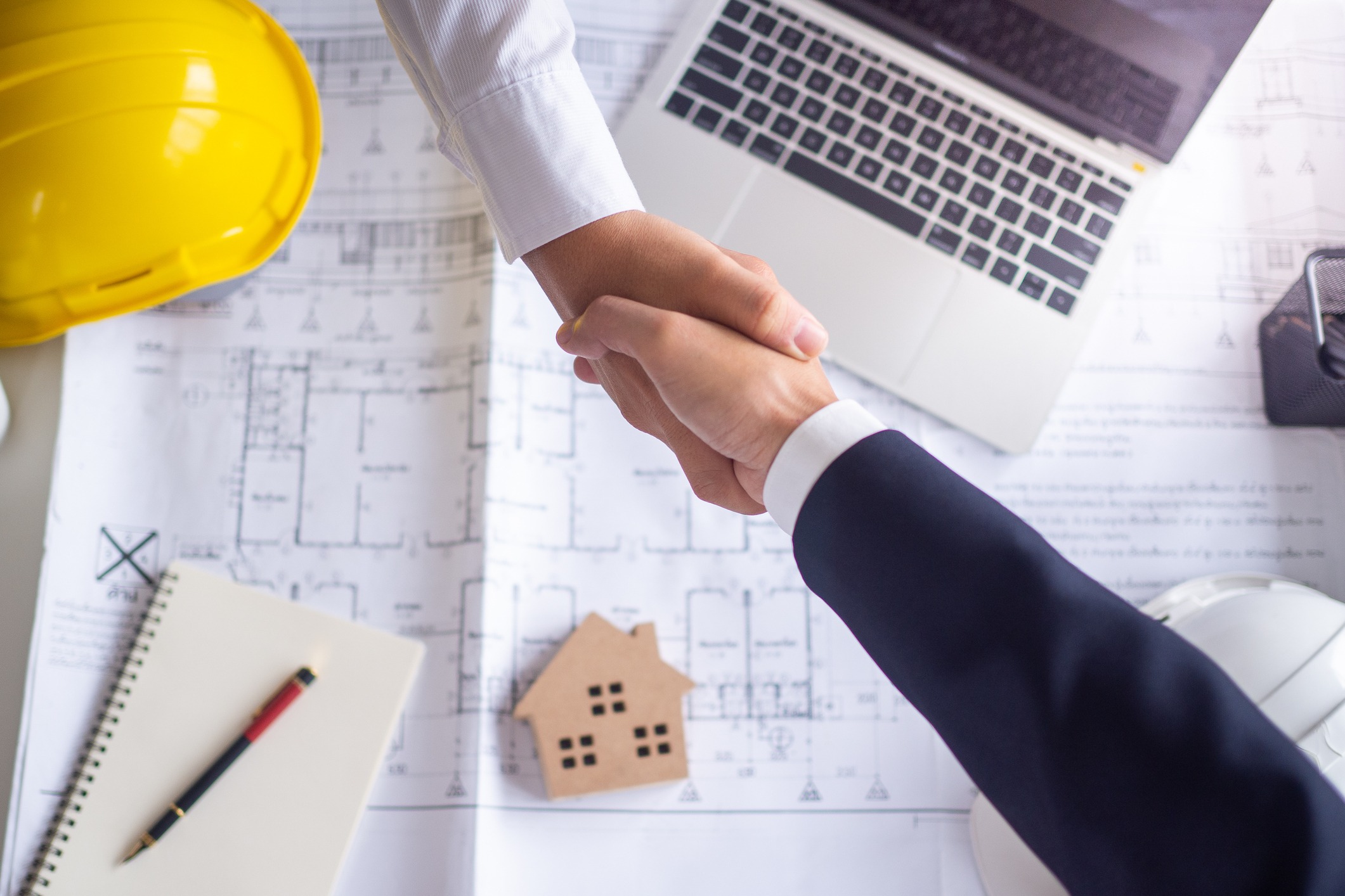 Handshake over blueprints with hard hat and laptop